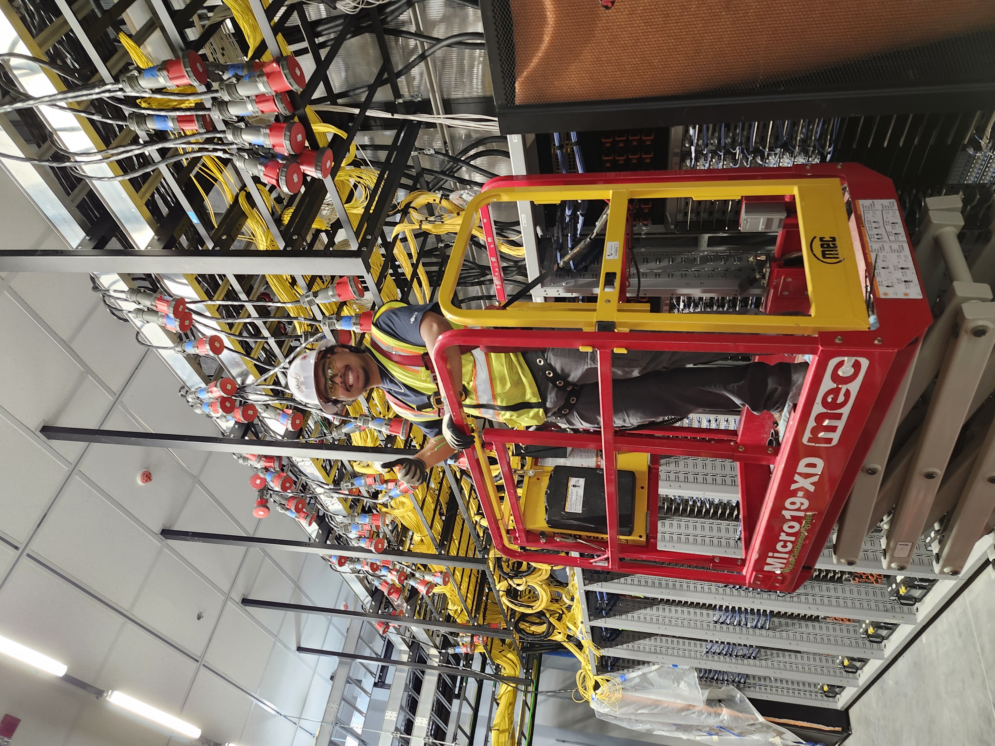 An AMP technician working from a lift among overhead cable trays in a data hall