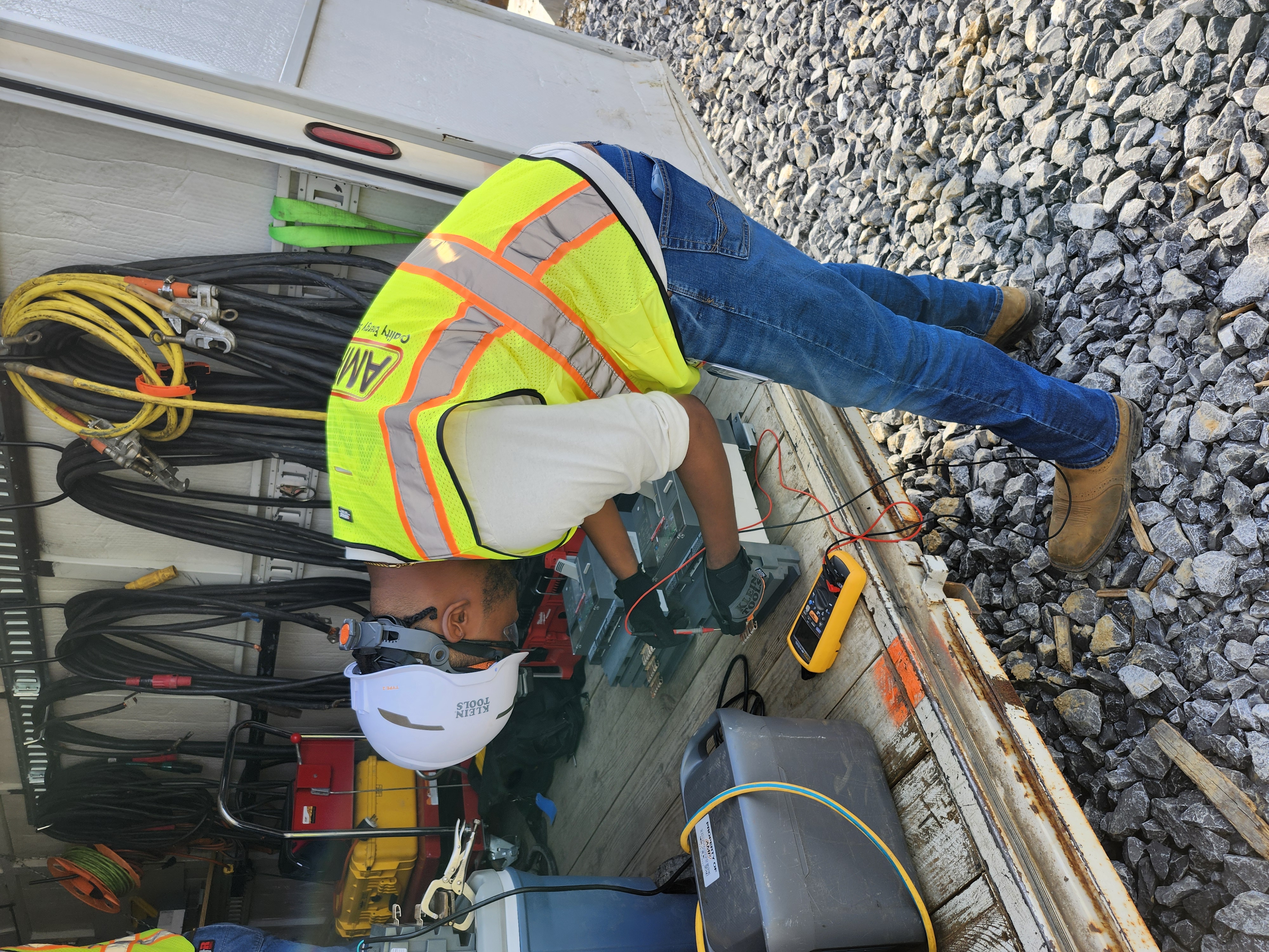 An AMP technician in hi-vis and a hard hat testing a breaker on a job site