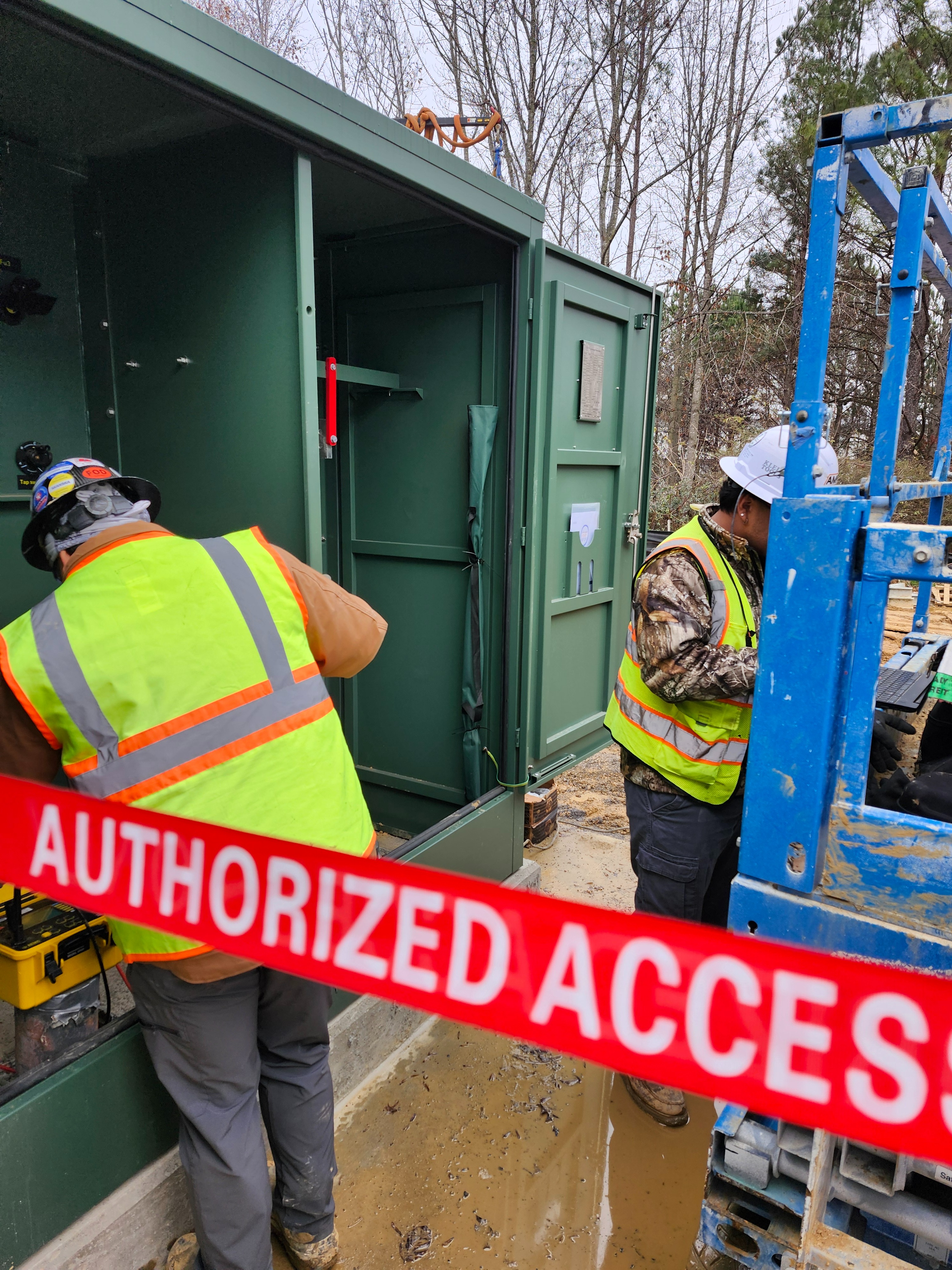 An AMP technician in arc-rated PPE connecting test leads to the high-voltage bushings of a padmount transformer
